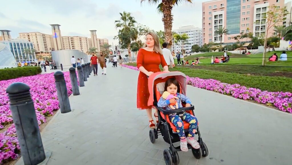 花が咲き誇るドバイの整備された安全な遊歩道で、子供を乗せたベビーカーを押す女性